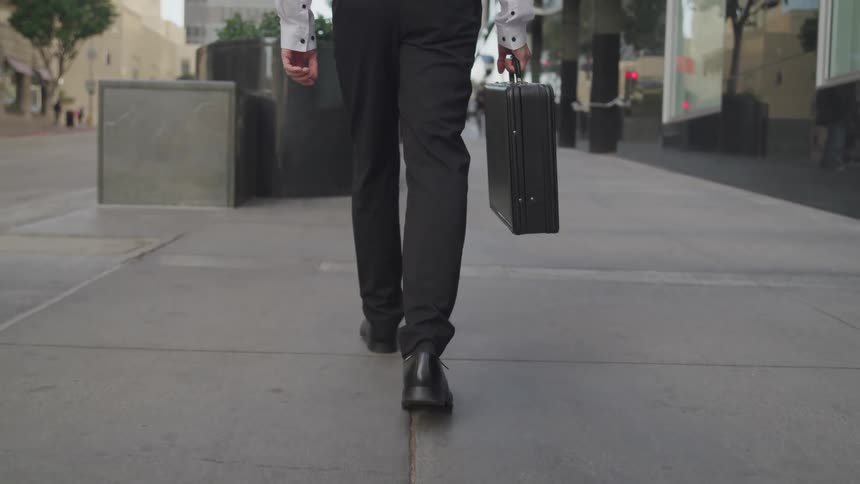 A man carries a briefcase walking a city sidewalk