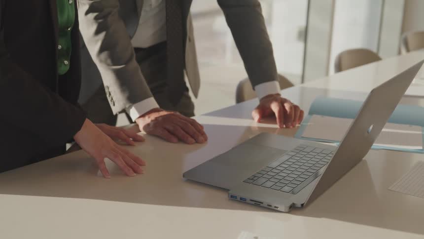 A pair of men stand in front of a laptop on a conference table and point at the screen