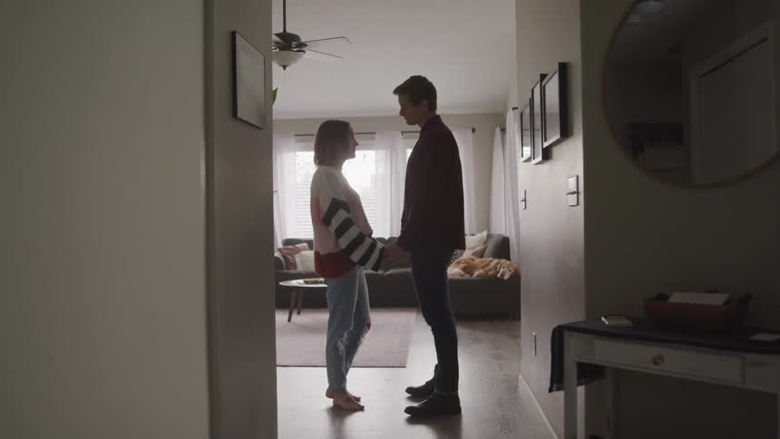 A man and woman standing in a house look at one another as they hold hands
