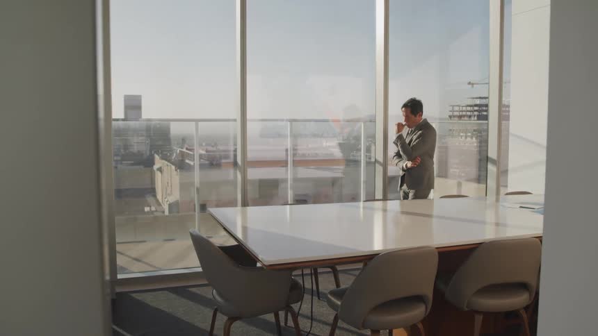 Asian businessman deep in thought walks and looks out the windows in the conference room