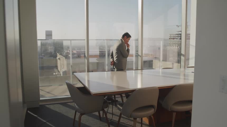 Man wearing a suit paces in an office next to a table
