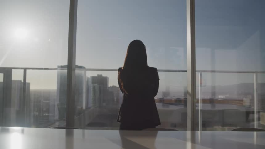 A woman is watching the city from the tall building window