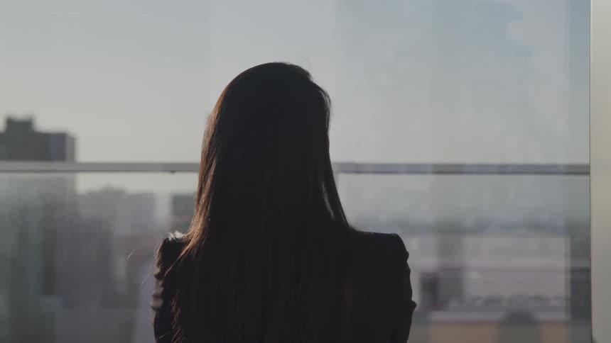Woman stands near window overlooking city downtown