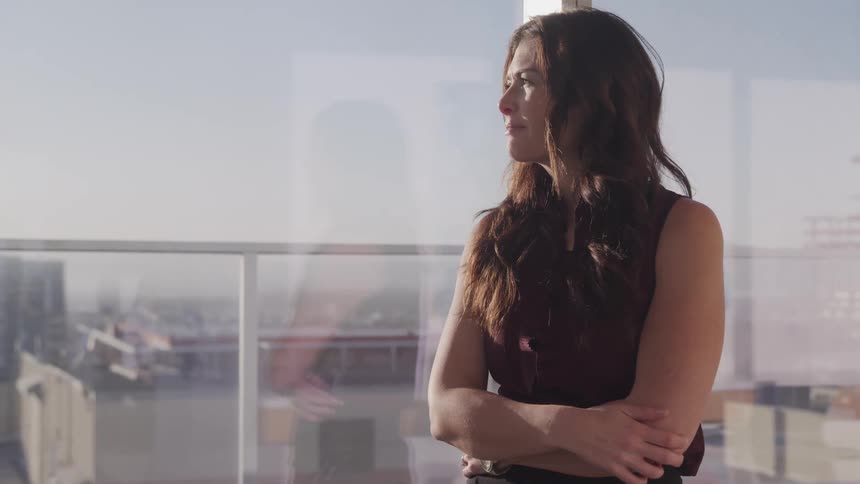 Businesswoman with black wavy hair looks out the office windows