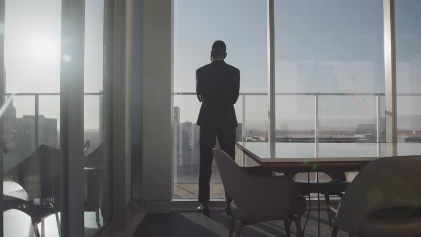 Black businessman with a beard and a suit looks out the office windows in the meeting room