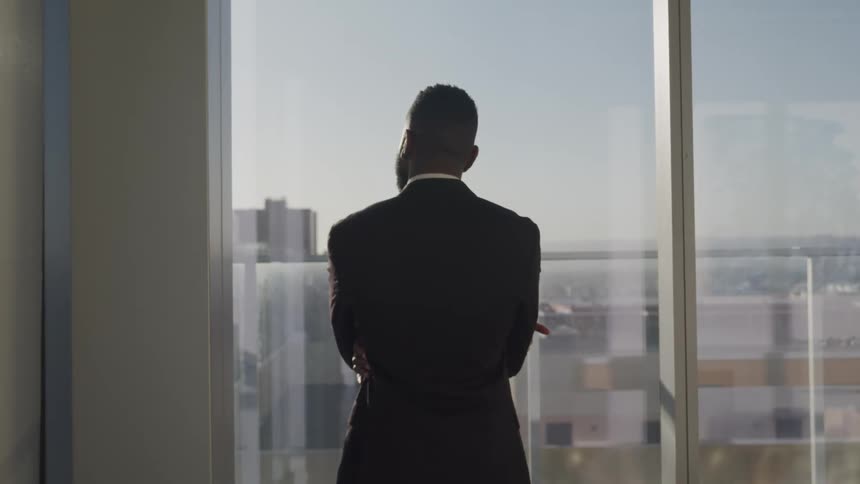 A man is standing in an office building and looking out the window