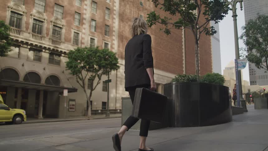 A woman carries a briefcase walking a city sidewalk