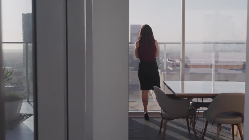 A woman is standing in an office and looking out the window