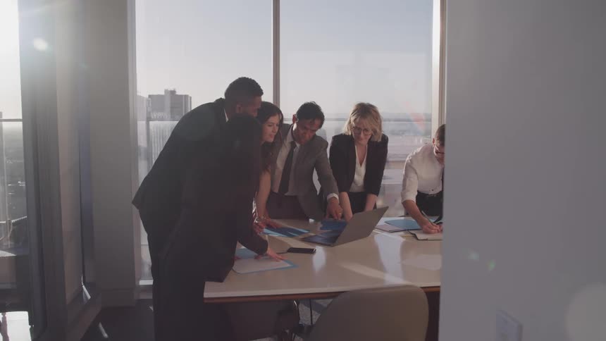 A group of coworkers in an office lean over a desk and look at a laptop