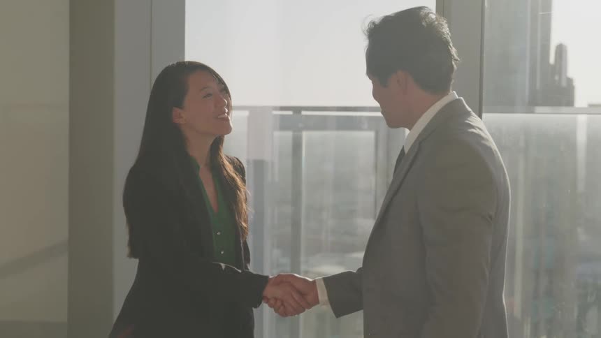 Asian businessman with a grey suit and businesswoman with a black blazer jacket shake hands in the office