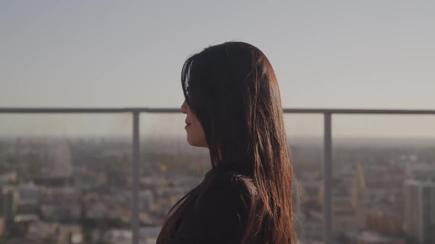 A woman in a blazer stands on a rooftop in a metropolis on a sunny day