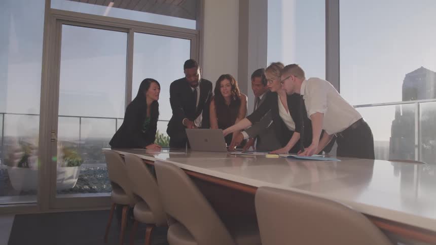 Business people consult standing over laptop set on conference table with view of city skyscrapers