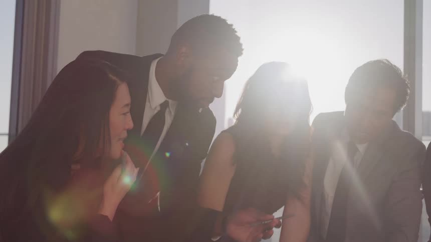Two men with suits and ties and three women in a conference room with a window in the background