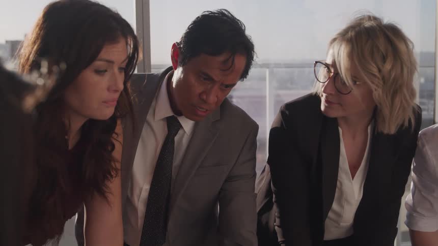 A group of people stand together in an office and gaze at something out of frame