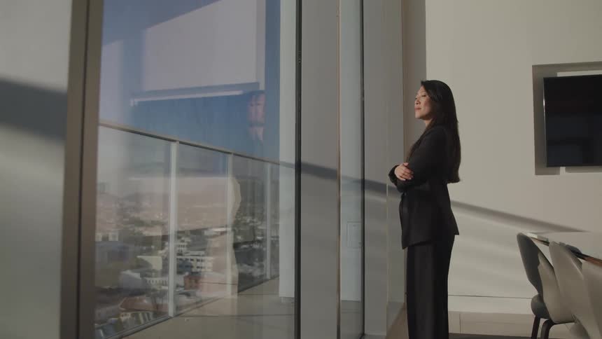 Asian businesswoman with a black suit looks out the office windows