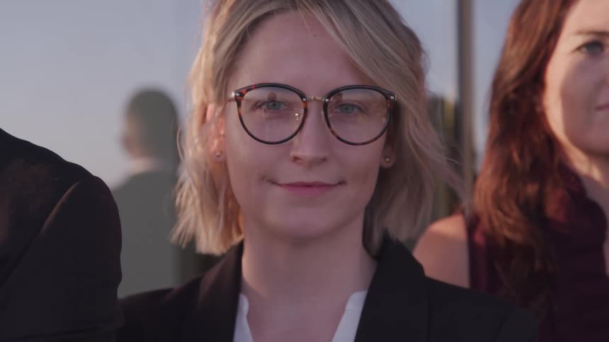 A woman with glasses staring and standing with a window in the background