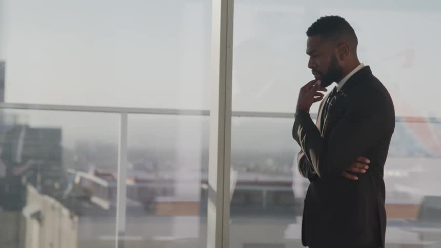 Businessman with a beard and a suit walks next to office windows in the meeting room