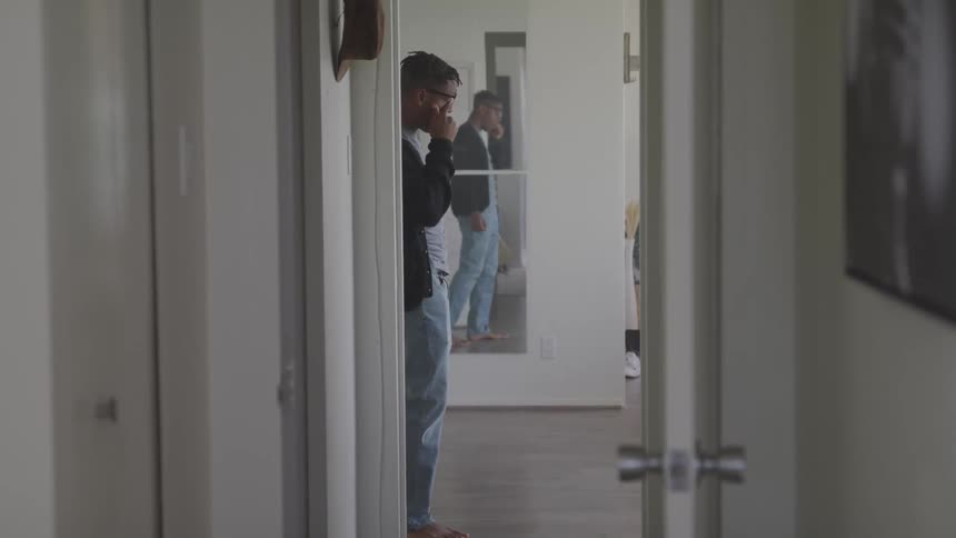 A man with glasses walking by a doorway with a mirror in the background