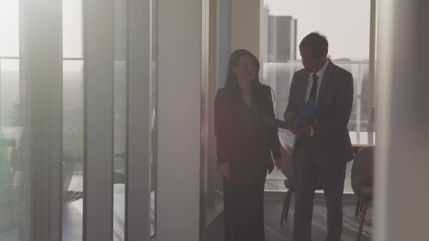 Business people talking over documents while walking on an office at sunset