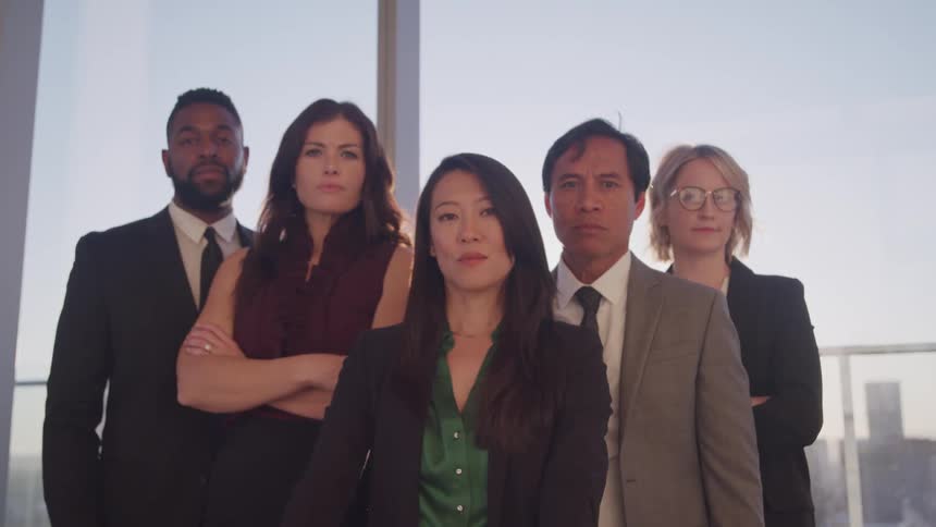 Business people stand for group portrait near window showing downtown skyscrapers