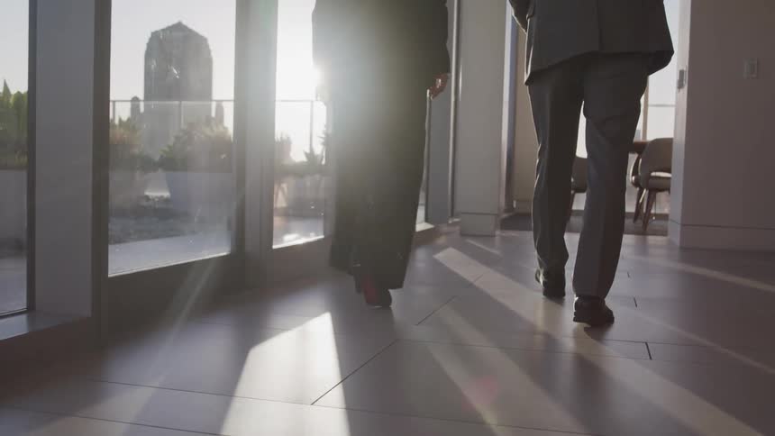 A woman and man in business attire walk next to large windows in a condo in a skyscraper on a sunny day