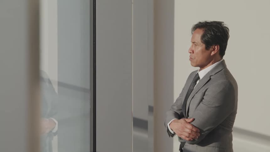 Asian businessman with a grey suit looks out the office windows