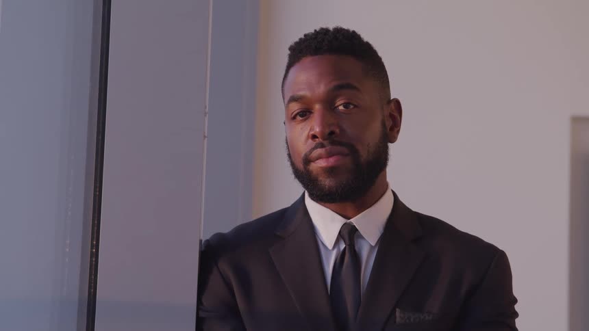 A man with a suit and tie standing next to a window with a door in the background