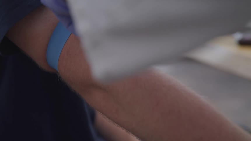 A doctor ties tubing around a patients arm as he prepares to give him a shot
