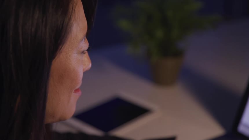 Side view of a middle aged asian woman using a laptop and smiling