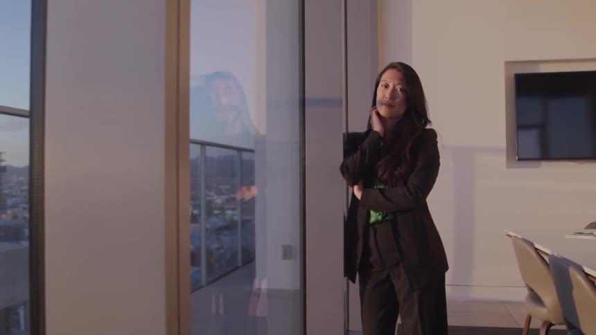 A woman stands and looks out her office window