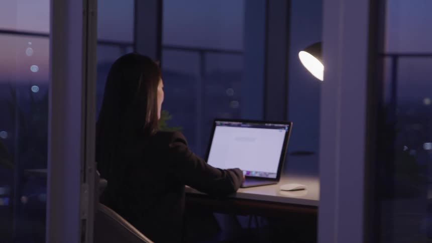 A woman working on her laptop in an office in the evening