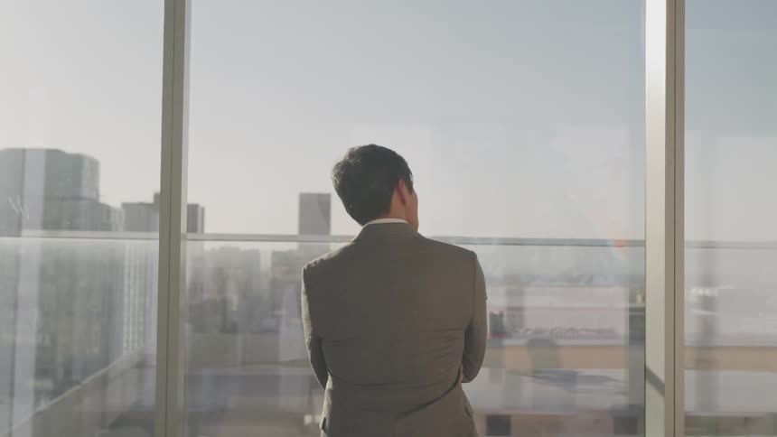 Businessman stands looking out at cityscape with arms crossed