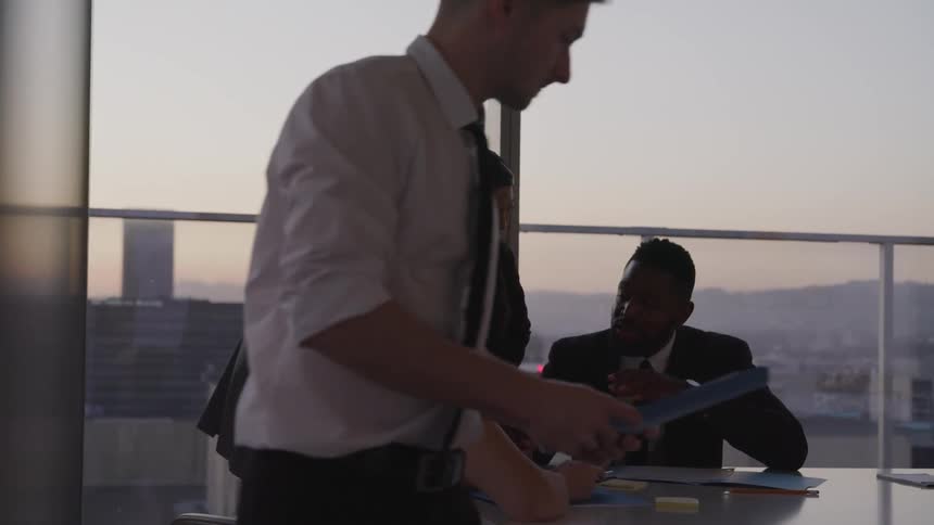 Business people holding a meeting in the office are silhouetted against the sky at dusk