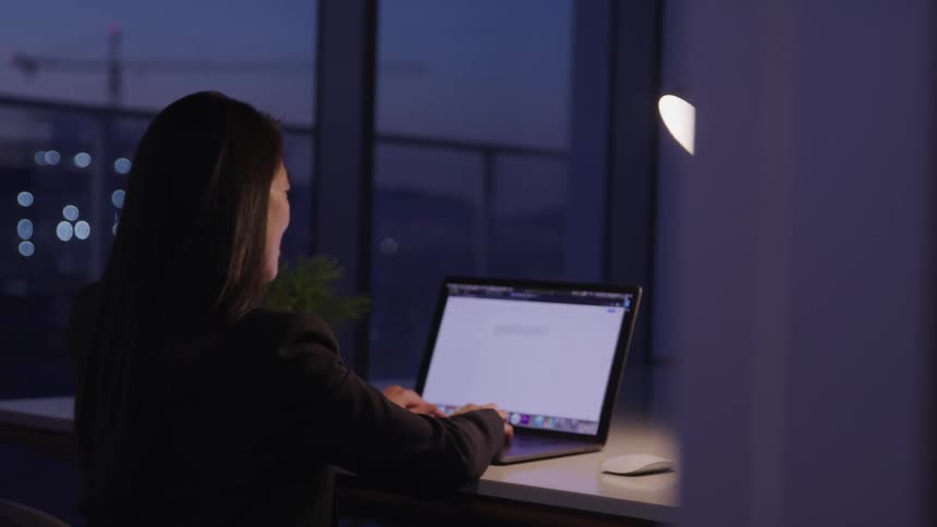A woman works on her laptop in her office at dusk