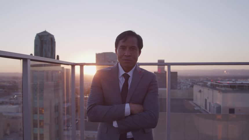 A man is standing on a balcony in a downtown area