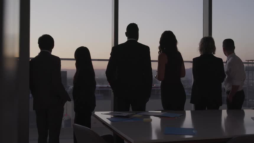 Business people stand and look out the office windows in conference room at dusk