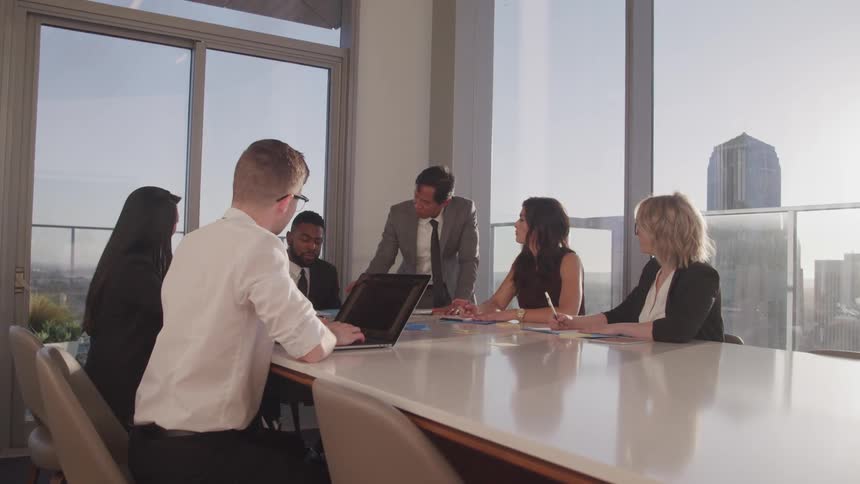 Business people sit at a long table conduct a meeting in conference room