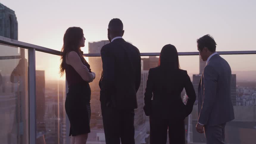 Group of business people looking at the city skyline at sunset from a balcony