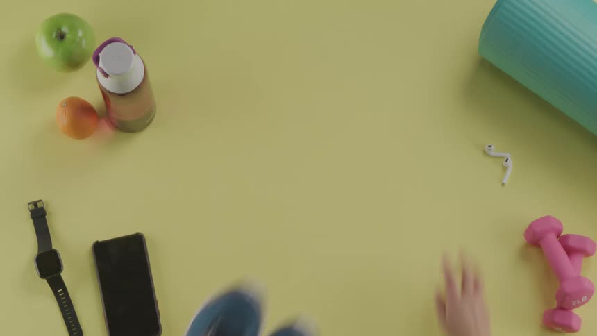Pair of hands grab some shoes and air pods that are sitting near a water bottle weights and cellphone