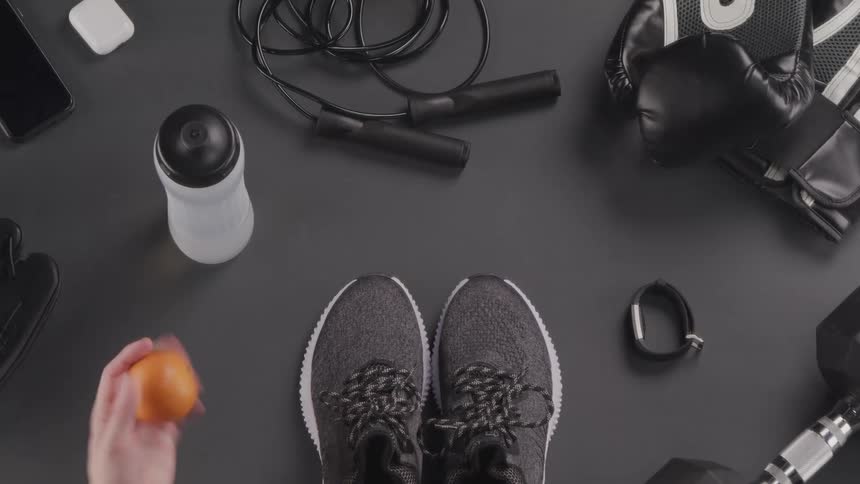 A woman picks up an orange that is lying next to exercise equipment