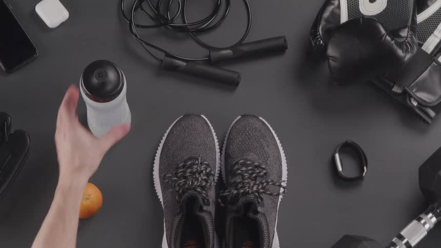 A pair of sneakers a water bottle an orange and other weight training items lit on a flat surface until the sneakers and water bottle are removed