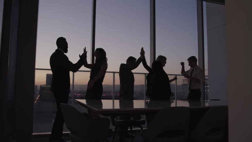 A group of people in a dimly lit office in the evening cheer and congratulate each other