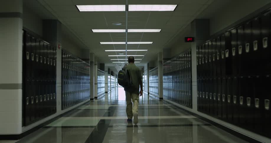 A young man walks down a wide hallway lined with lockers