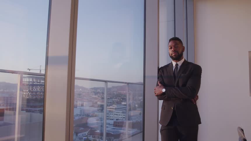 A man in a suit and tie standing next to a window and chairs