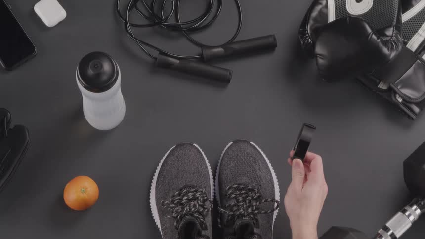 A person picks up a watch and sneakers from a table filled with sporting accessories