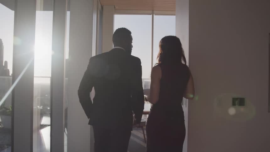 Black businessman with a beard a black suit and white businesswoman with wavy hair and a black skirt walks to the meeting room together