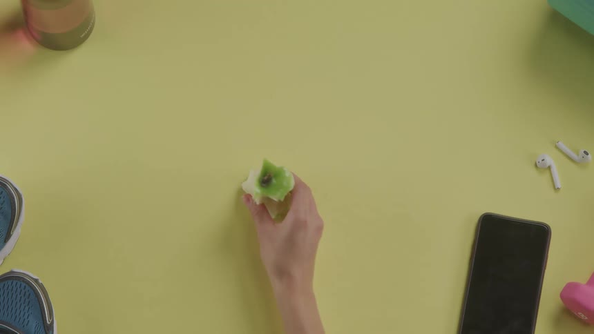 A woman places an eaten apple on a table near her smartphone shoes and weights