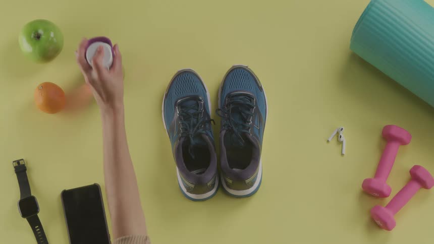 Woman picks up water bottle and hand weights from among other workout gear