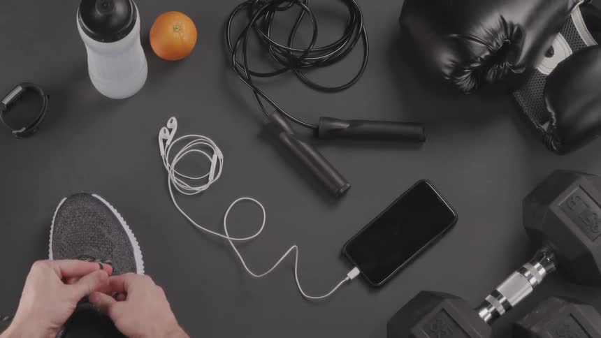 A person tying their shoelaces next to a smart phone and a jump rope