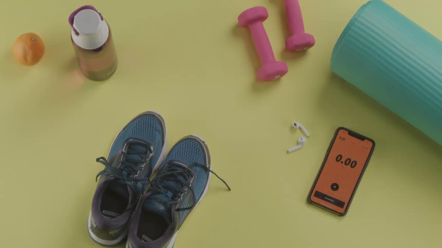 A number of items needed for a workout including weights and a yoga mat are all placed on a colorful surface